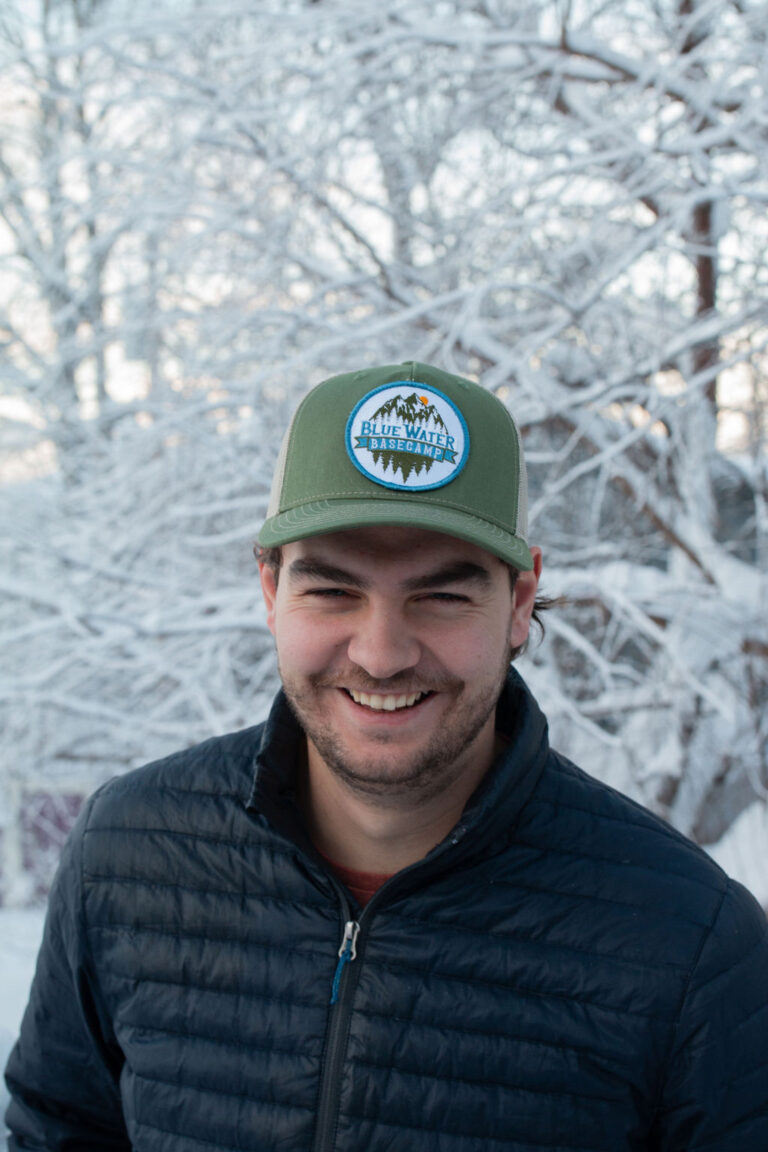 Smiling man wearing a Trucker cap in olive with BlueWater BaseCamp Logo on the front.