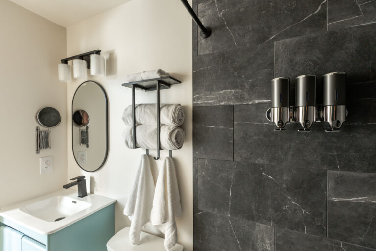 Dark tiled shower with sink, mirror and towel rack in background